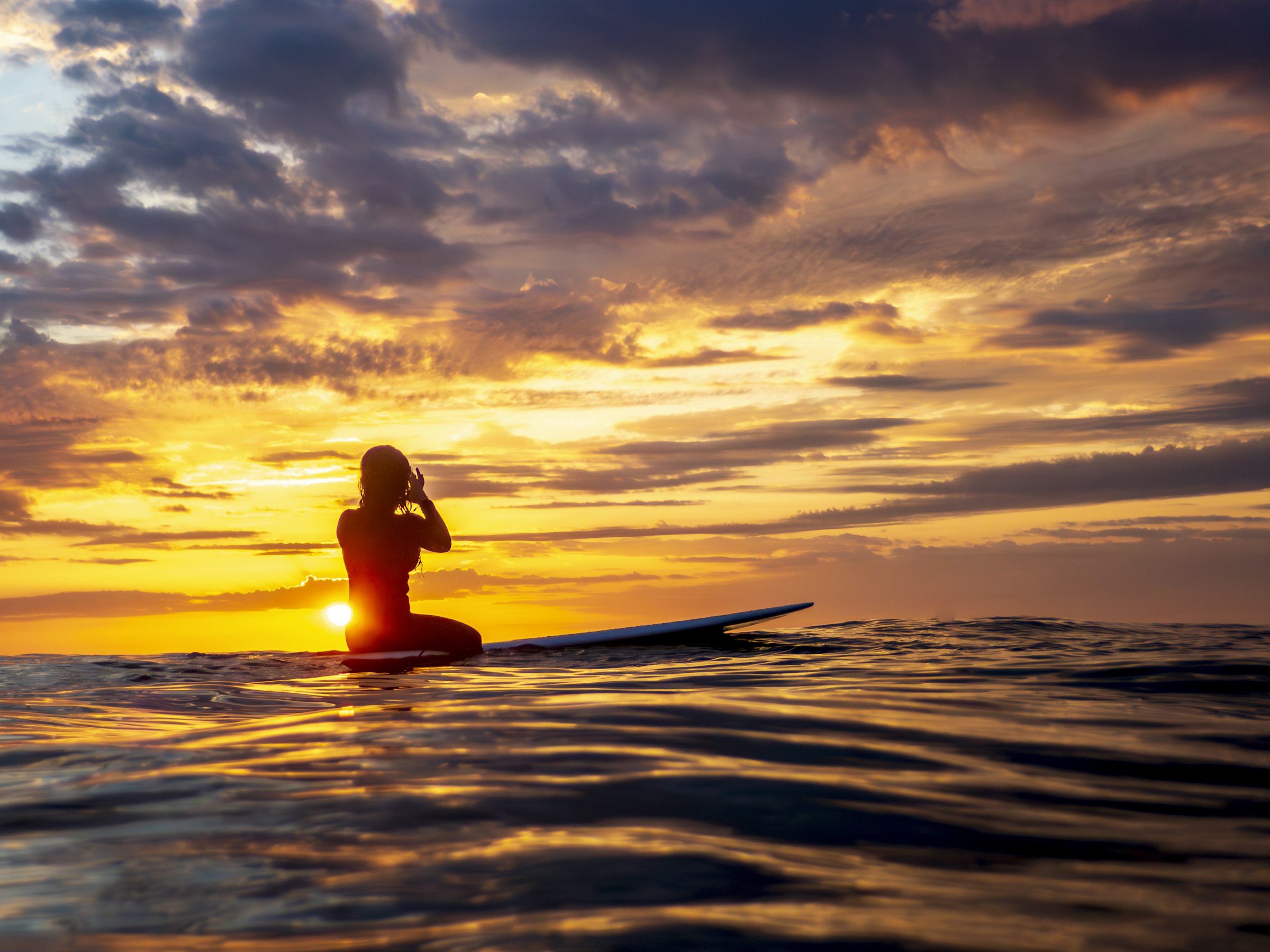 Surfer sitting on a board at sunset
